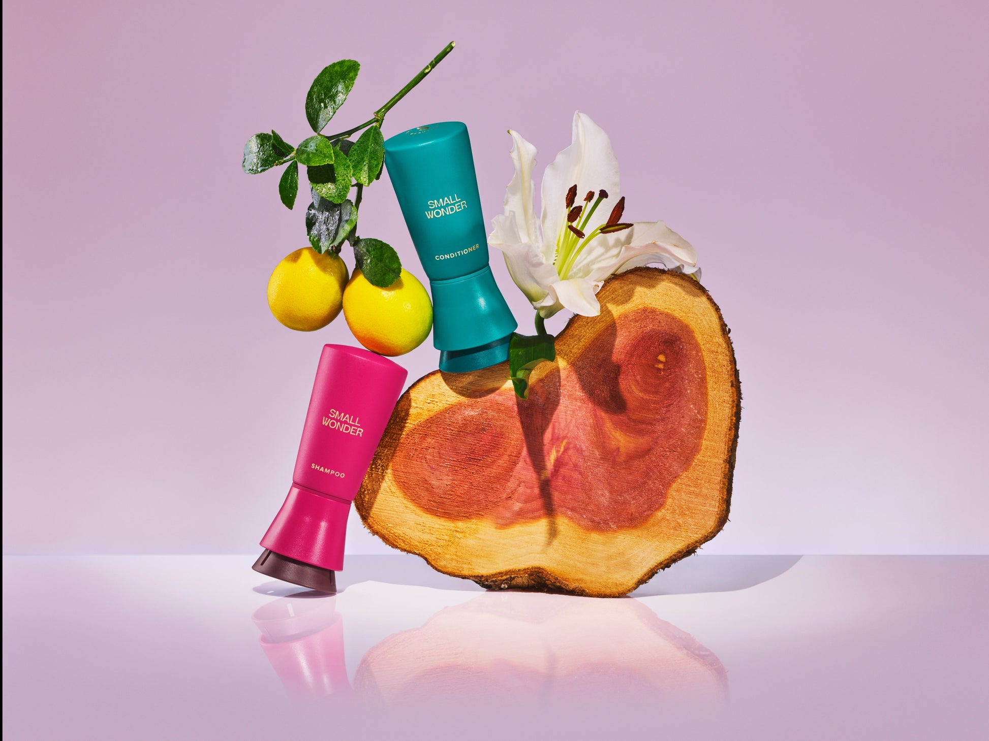 Small Wonder Shampoo & Conditioner dispense bottles next to lemons, a lily, and cedar wood
