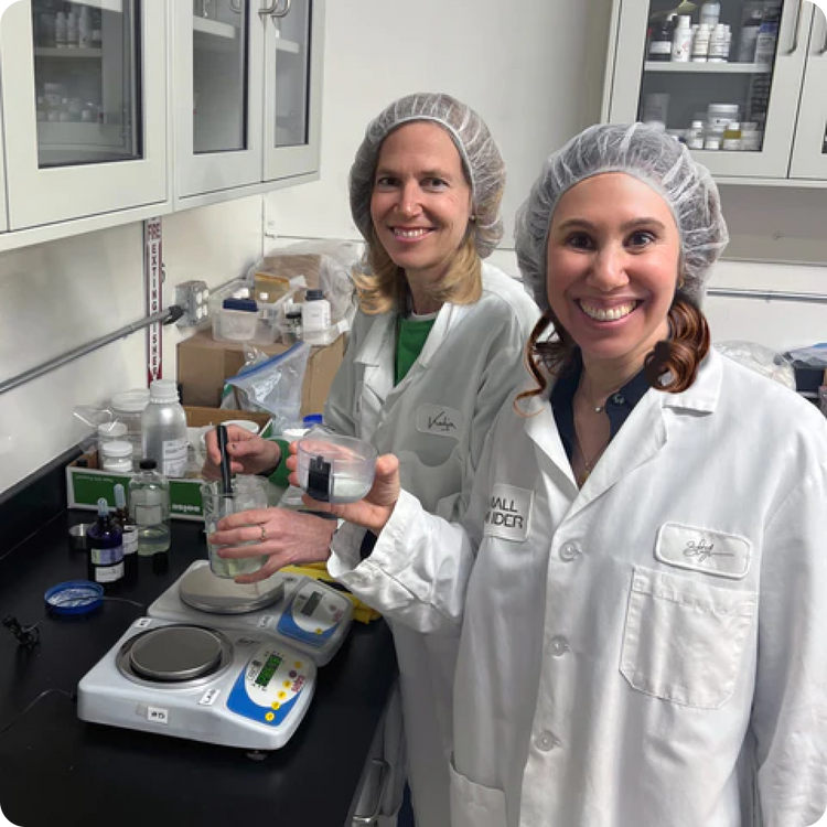 Two women in a lab wearing Small Wonder lab coats holding beakers
