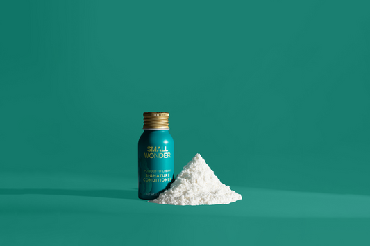 Bottle of 'Small Wonder' Signature Conditioner with a pile of white powder on a green background