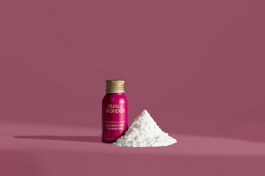 Small bottle of Small Wonder Signature shampoo with a pile of white powder on a pink background
