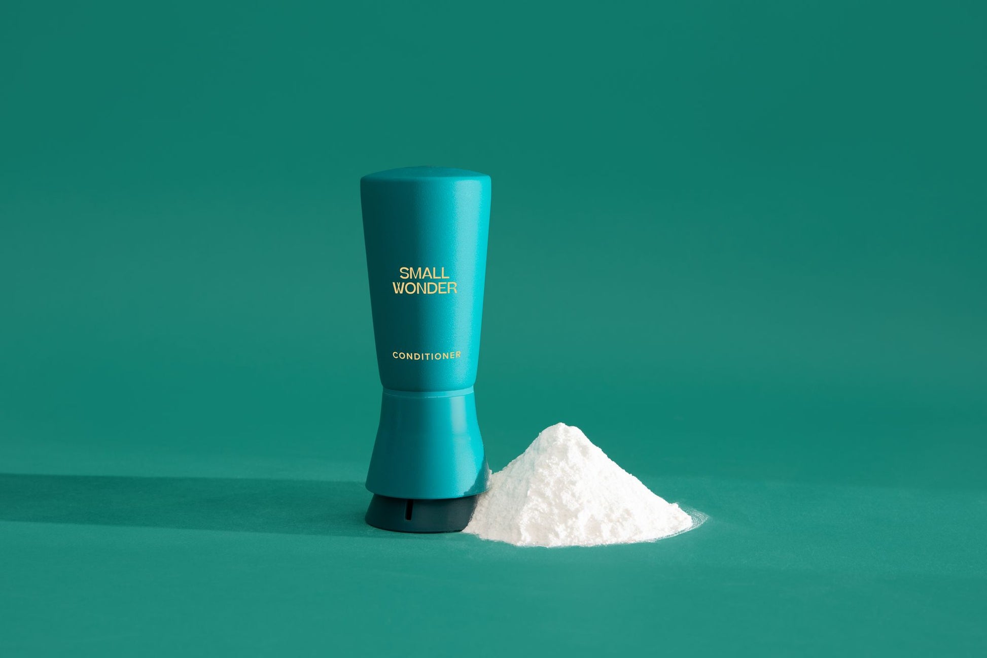 Teal cylindrical container labeled 'Small Wonder Conditioner' on a green background & white powder